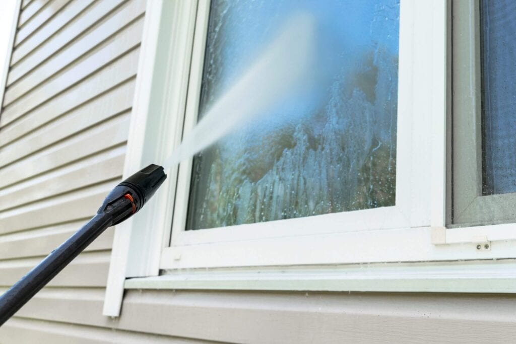 Professional pressure washing service cleaning vinyl siding and a residential window
