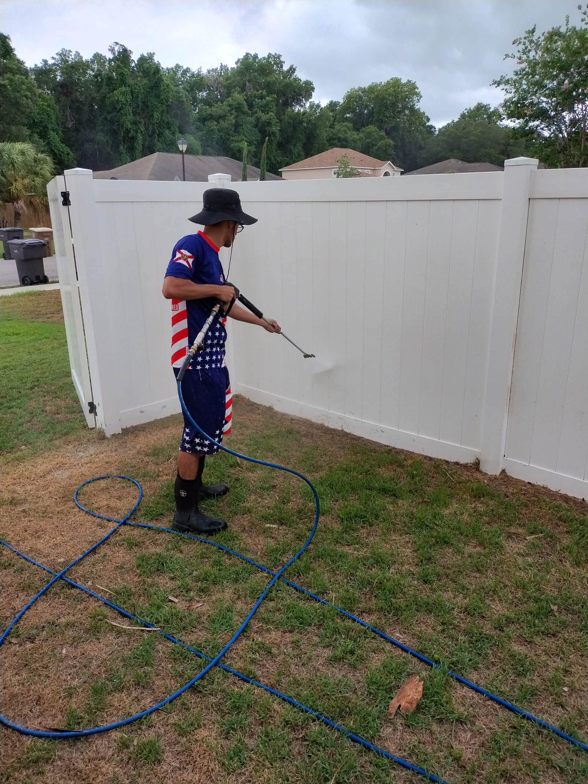 Man pressure washing a white vinyl fence