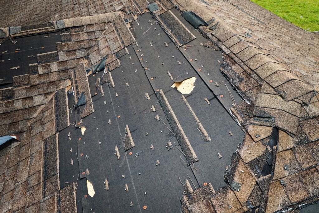 Close-up of a residential roof with missing asphalt shingles and exposed underlayment after a storm, illustrating the need for emergency roof repair in Central Florida.